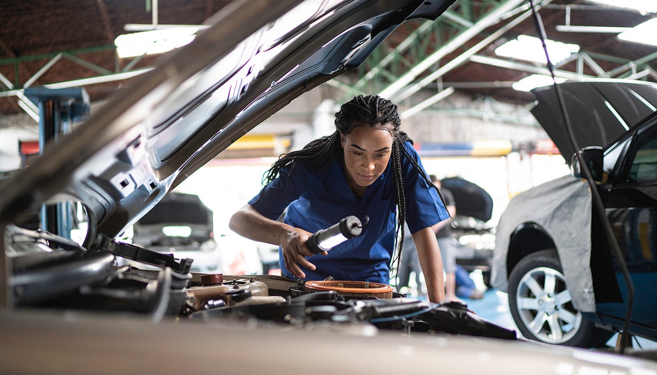 A female mechanic looking intently under the hood of a car