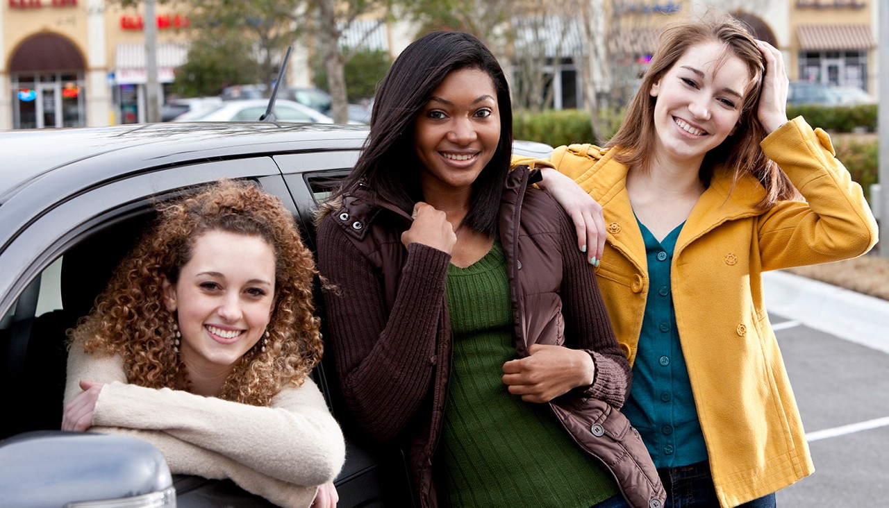 Three teen girls standing beside a car.