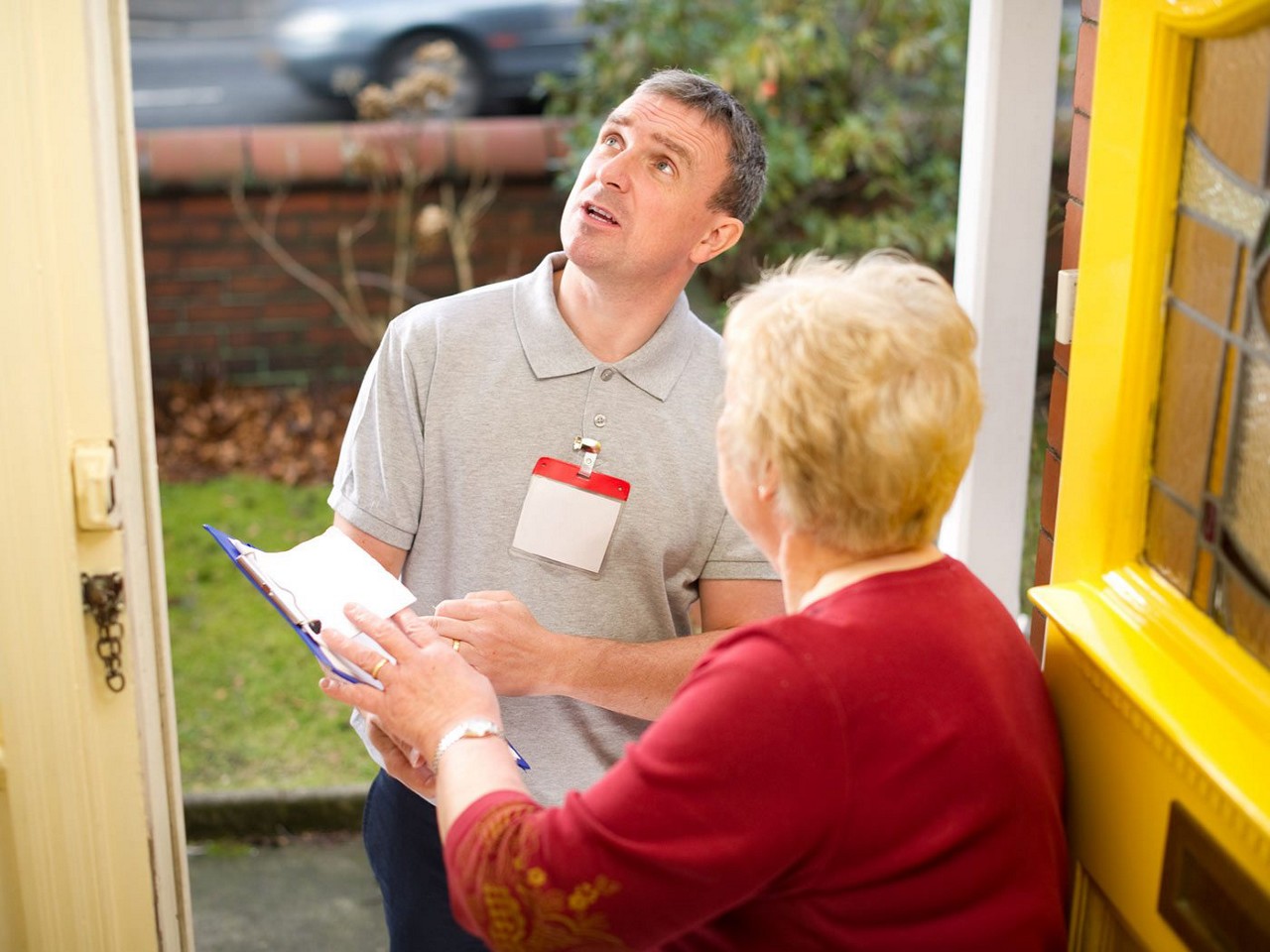 A man at the door with a name tag on talking an older woman and looking up at the roof.