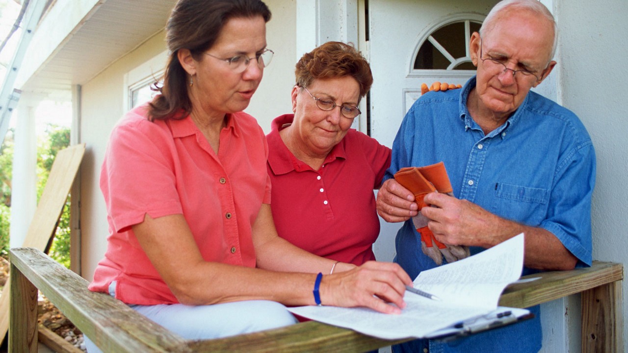 An insurance agent sharing paperwork with an older couple on their front porch.