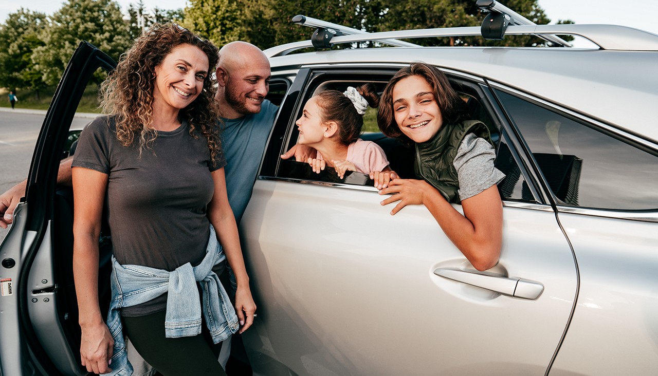 A family of four standing near their car with a roof rack on top.