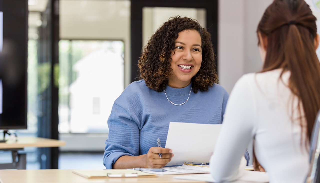 A woman sitting across from another woman holding paper.