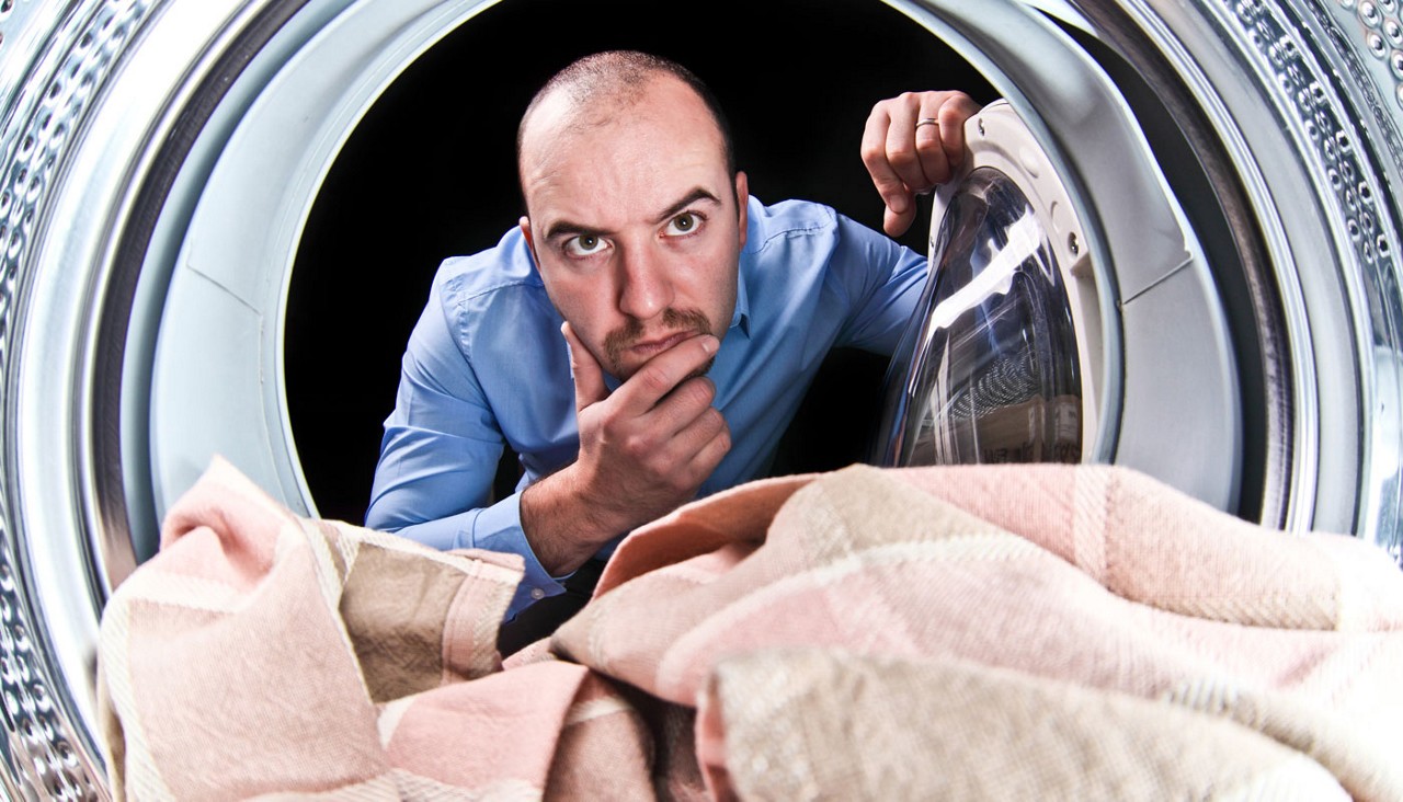 Man looking into a clothes dryer, confused