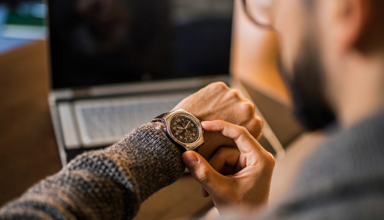 A man checks the time on his watch while seated at his desk.