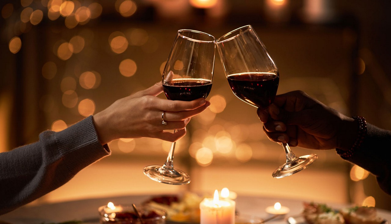 Close up of two people clinking wine glasses at dinner table