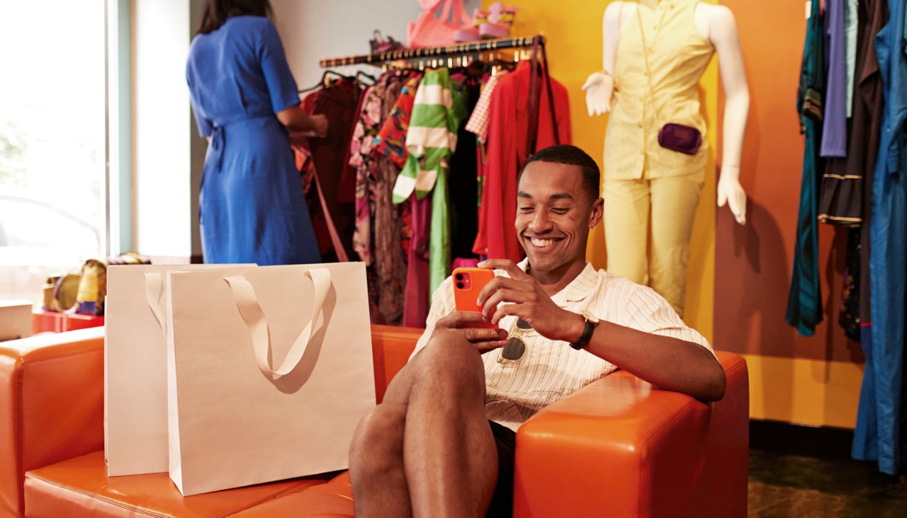 Happy young man using mobile phone on sofa in store
