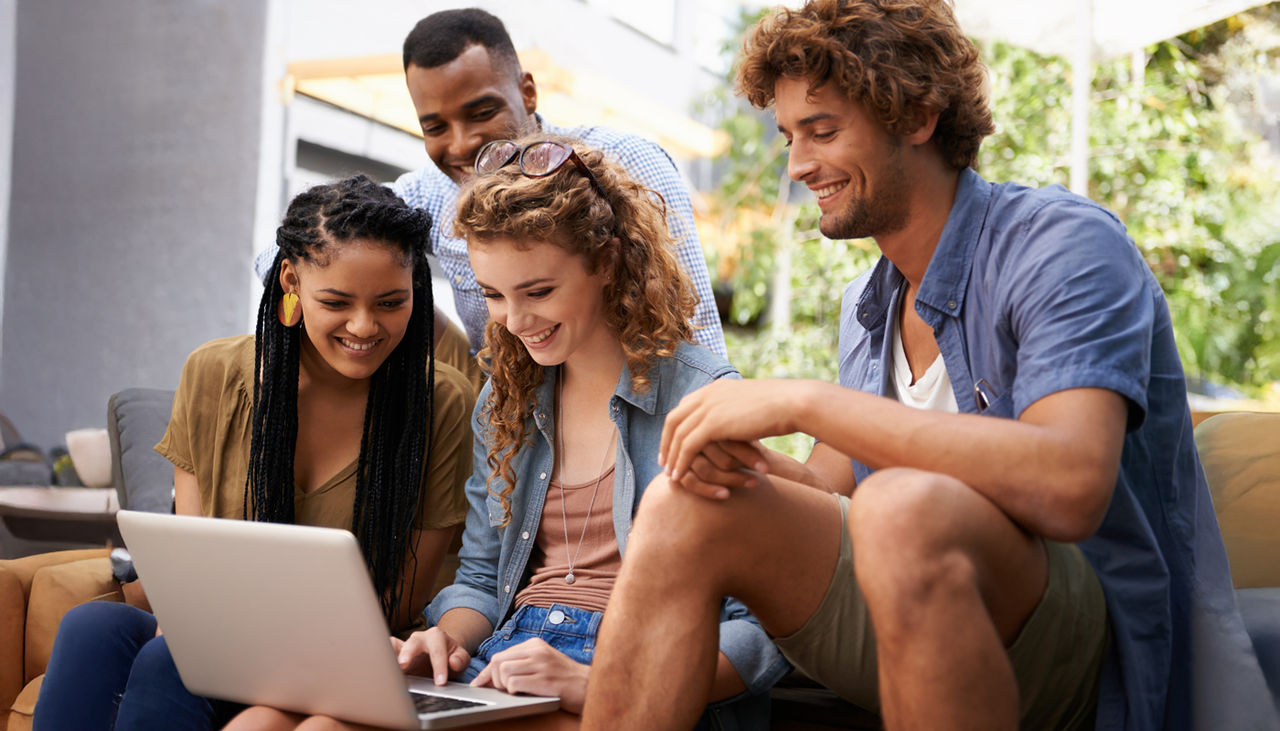 Group of young friends smiling as they look at laptop