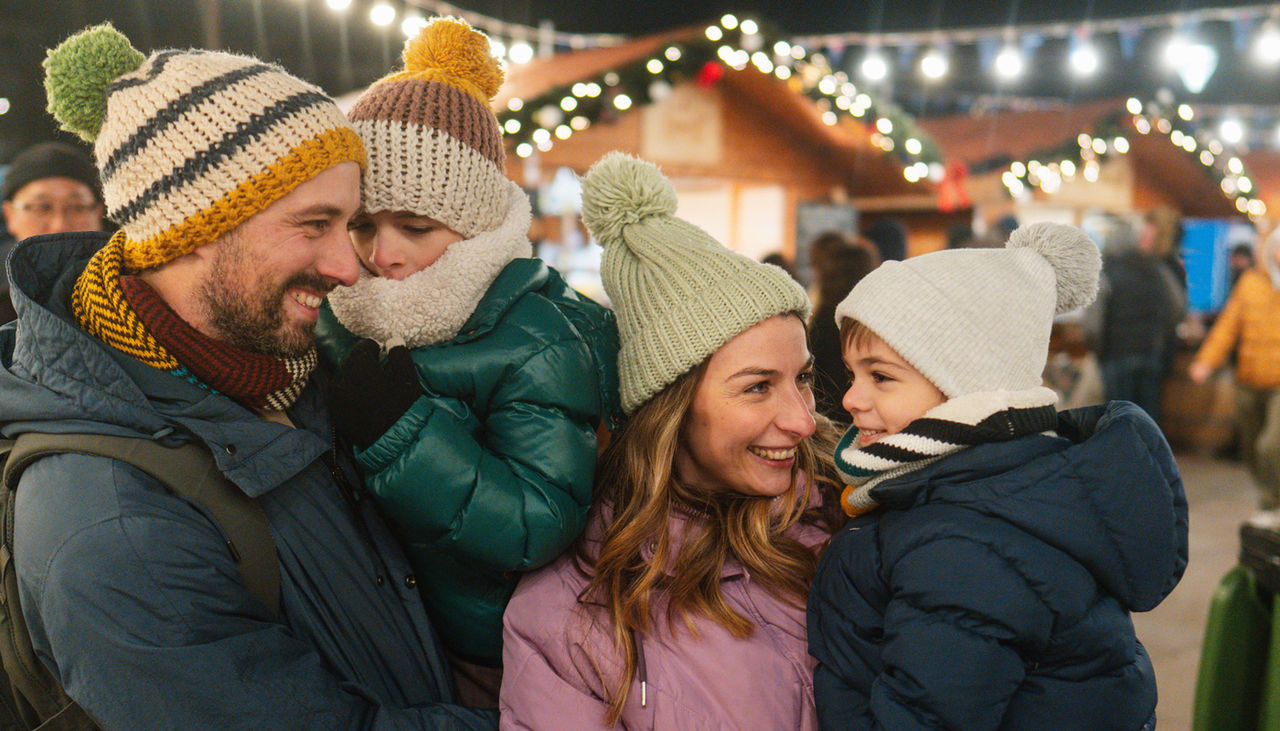 A young family with winter clothes and hats on outside at a festival.
